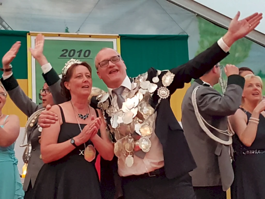 Eine festliche Szene beim Schützenfest in Freren: Ein strahlendes Paar, umgeben von fröhlichen Teilnehmern, feiert den Höhepunkt des Festes. Der Mann trägt eine beeindruckende Medaillenrobe, während die Frau elegant gekleidet ist. Die Atmosphäre ist von Freude und Gemeinschaft geprägt.