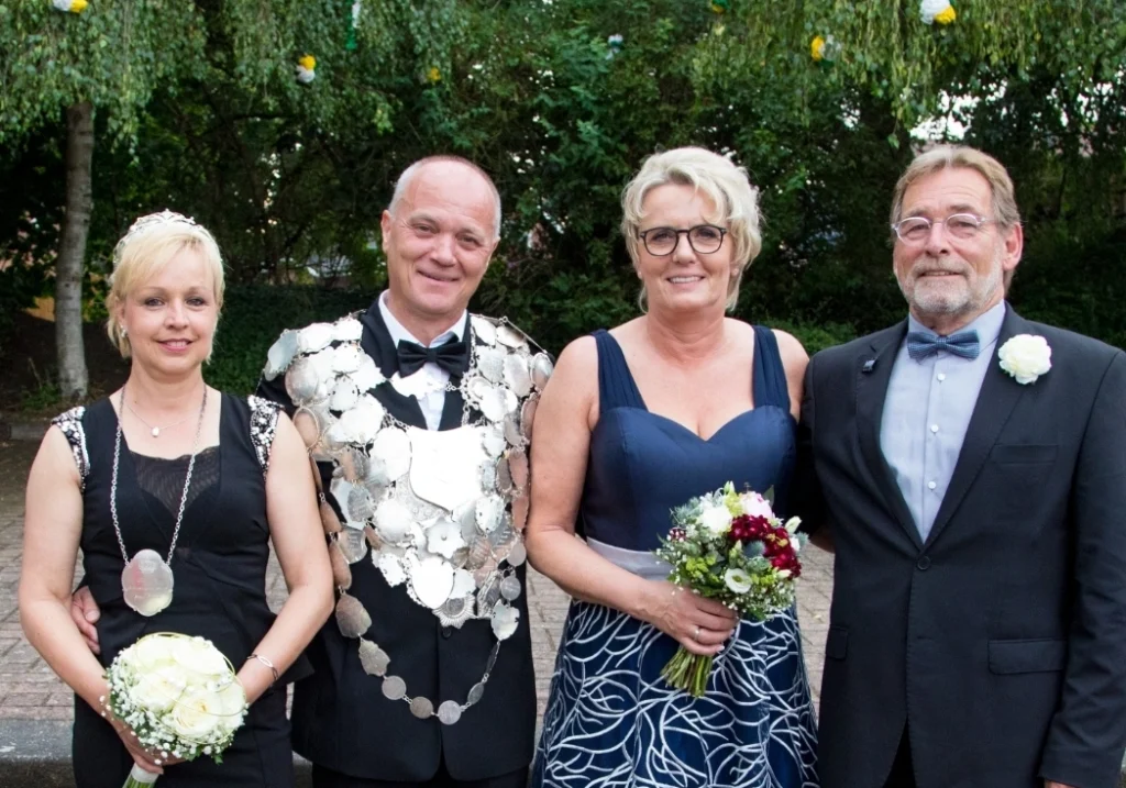 Festliche Stimmung beim Schützenfest in Freren: Vier Personen in eleganter Kleidung posieren fröhlich im Freien, umgeben von grüner Natur. Ein Höhepunkt der Schützengesellschaft, der Tradition und Gemeinschaft feiert.