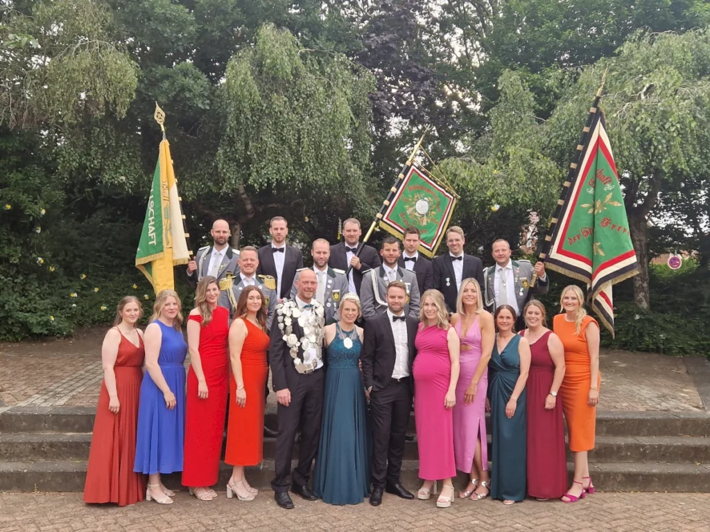 Gruppenfoto der Schützengesellschaft Freren: Mitglieder in festlicher Kleidung posieren mit Fahnen vor einer grünen Kulisse. Ein Highlight des Schützenfests, das Gemeinschaft und Tradition feiert.